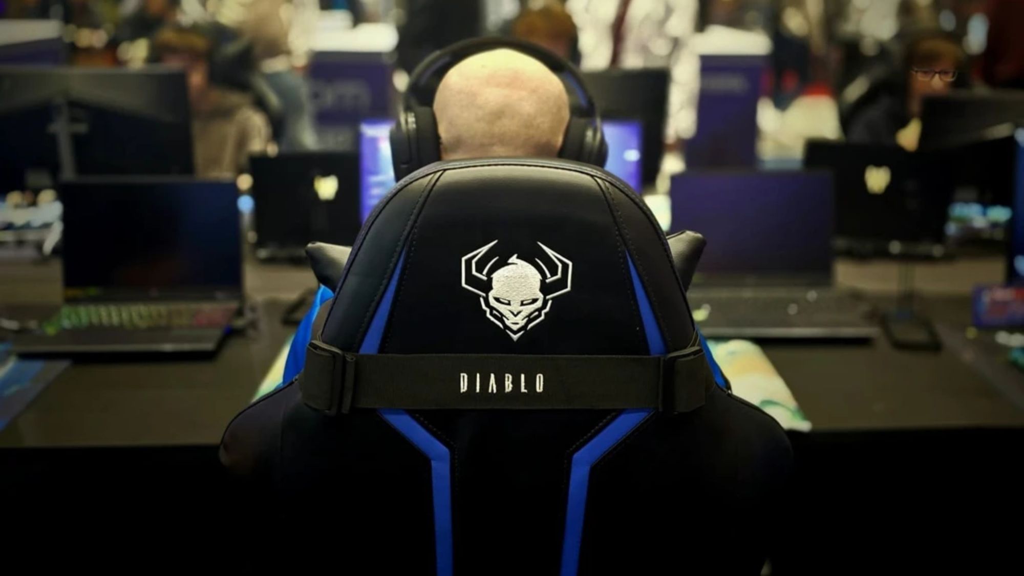 Účastník IEM 2026 so slúchadlami na čierno-modrej stoličke Diablo Chairs