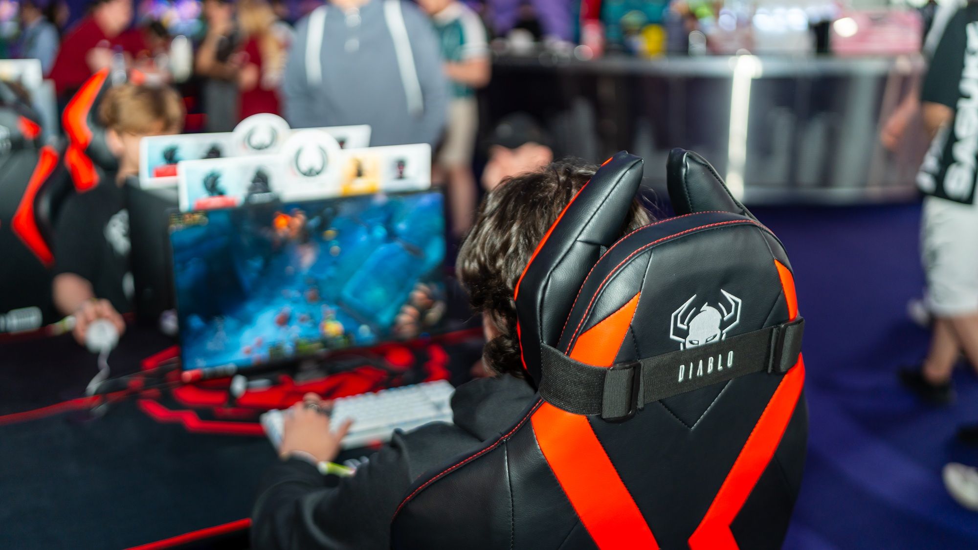 Hráč za červeno-čiernou stoličkou pri stanovišti na Rift Legends